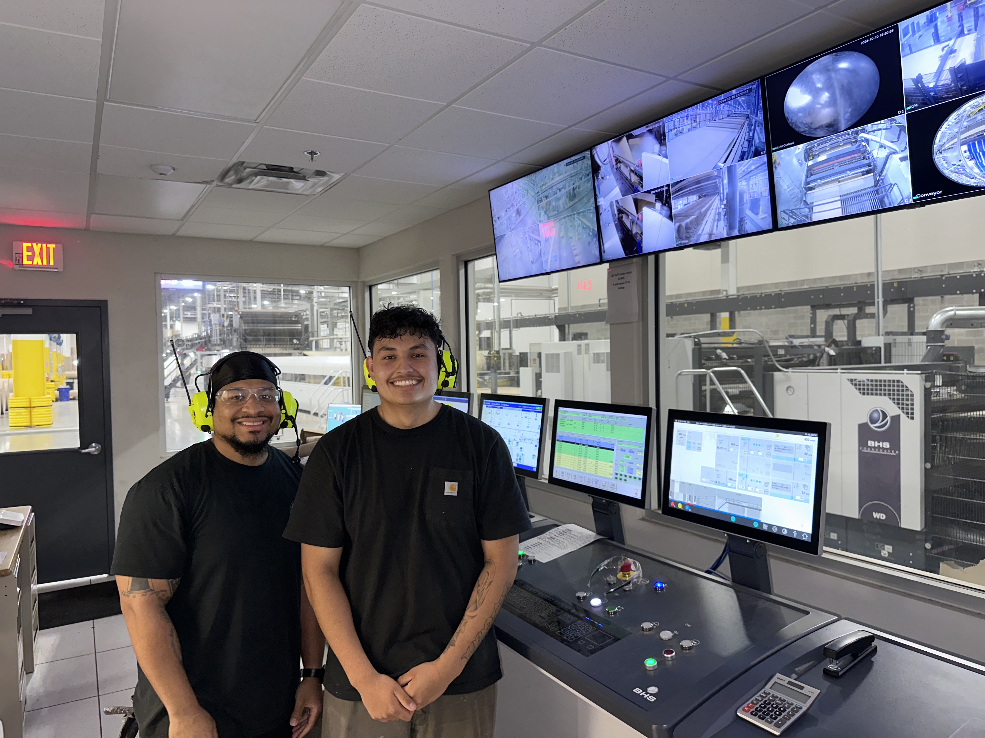 two men standing in front of a control room with monitors