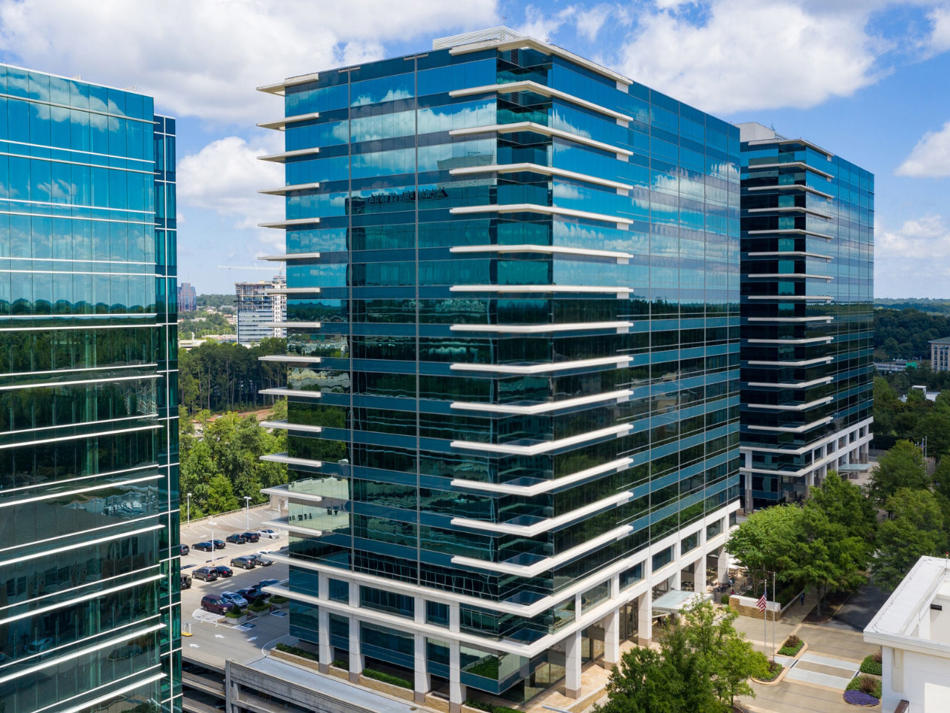 a tall glass building with trees and a street in the background